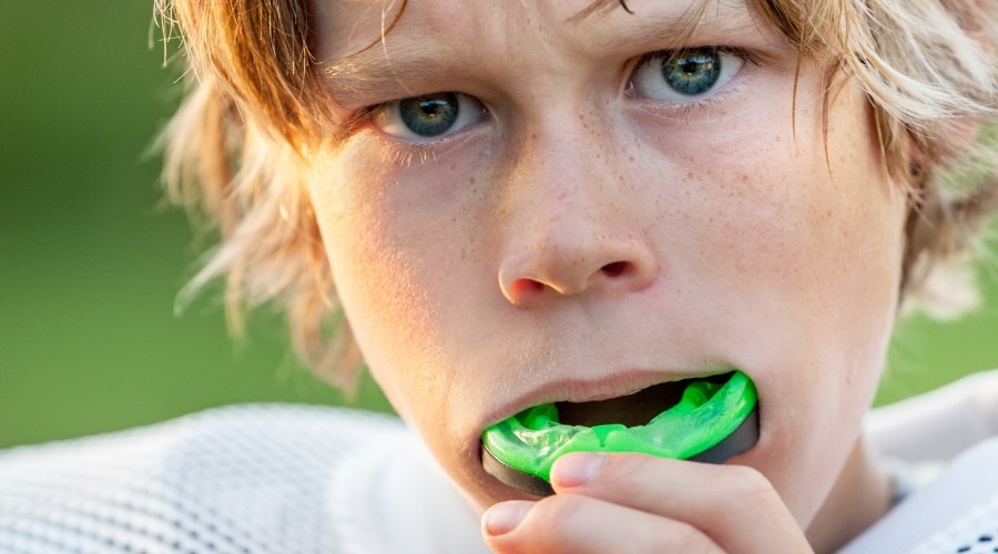 Young boy placing green athletic mouthguard in Southampton over his teeth