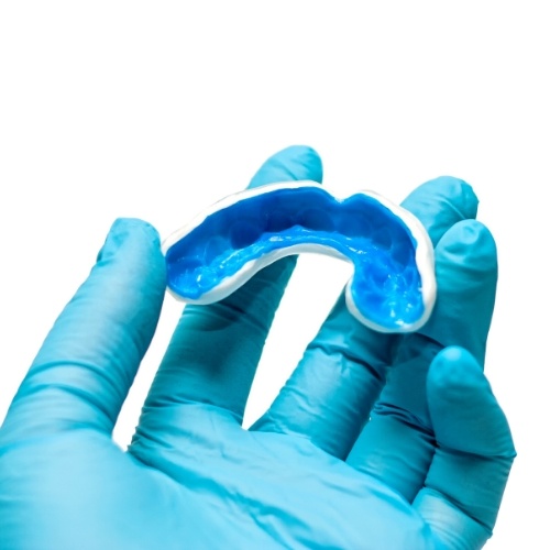 Gloved hand holding a blue athletic mouthguard