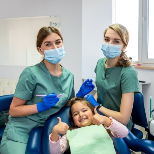 Two dental team members with young girl giving thumbs up