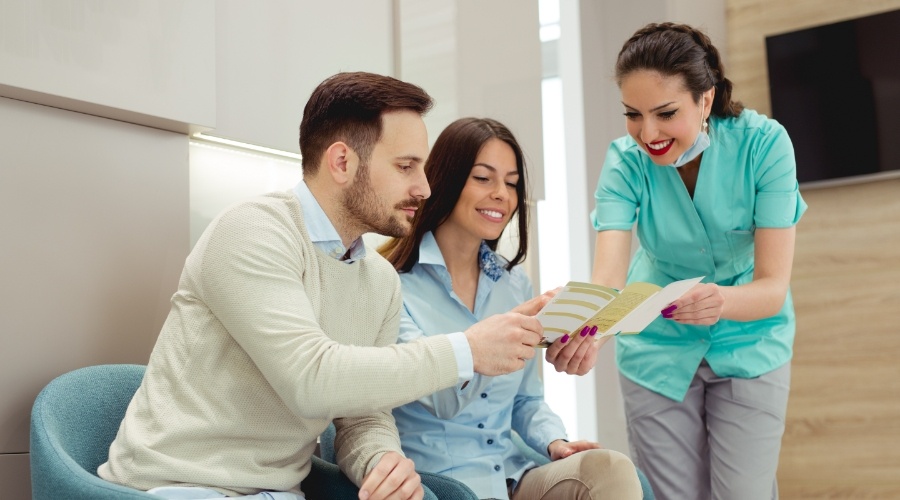 Dental team member showing dental insurance pamphlet to mand an woman