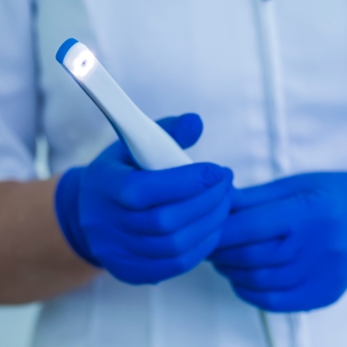 Gloved hands holding a thin white intraoral camera