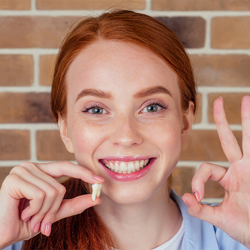 Young woman holding an extracted tooth and making okay sign with her other hand