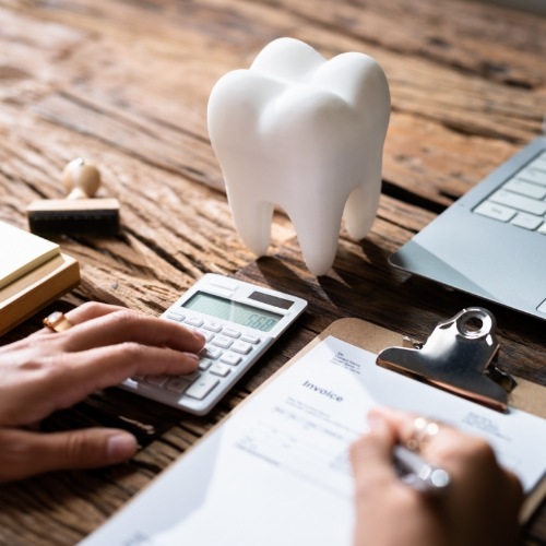 Person typing on calculator next to clipboard and model of tooth