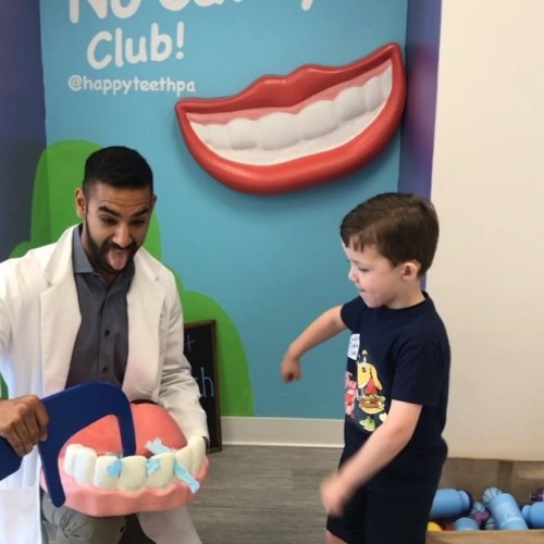 Doctor Singh joking with young boy patient while flossing giant model of teeth