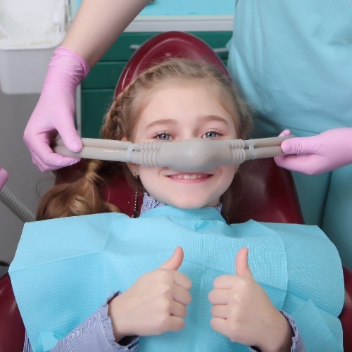 Young girl with nitrous oxide mask giving thumbs up in dental chair